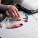 foto de muestrario de esmalte de uñas de muchos colores, con una mano y una lámpara fara curar el esmalte